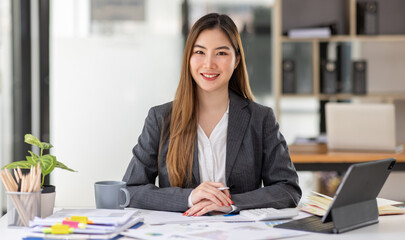 Young business Asian woman is sitting at table, working on laptop with graphs, charts, money and report financial concepts. Online marketing, education, analytics, e-commerce, business planning