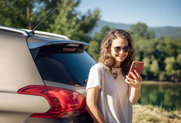Happy young woman driver traveler in sunglasses using smartphone during summe adventure travel