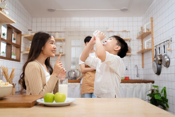 Asian cute little boy having a breakfast with his parent in a kitchen, boy holding a glass of milk...