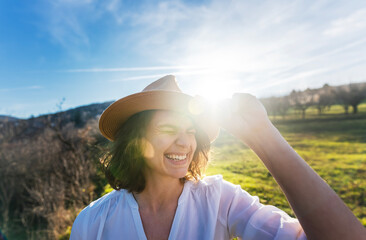 Young happy pretty smiling caucasian woman in a hat enjoys the sun while standing in a green spring field