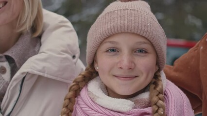Portrait of pretty 12 year old ginger girl smiling at camera standing in winter forest being kissed on both sides by her parents