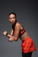 tattooed african american sportswoman in red sports bra working out on grey.