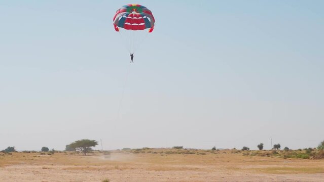 Wide angle shot of an Indian man enjoying parasailing in the Thar desert at Jaisalmer in Rajasthan, India. Indian tourist enjoying adventure activities in the desert. Man enjoying parasailing.