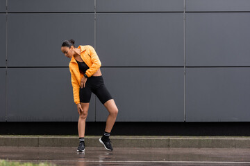 full length of african american sportswoman in stylish sneakers and yellow puffer jacket posing outside.