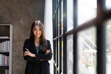 Young business woman standing to drinking coffee and thinking about the strategy of new startup while looking out the window in modern office.