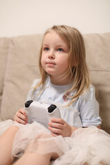 Kids Gaming video games concept. Toddler or young girl playing game with joystick, enjoying games, sitting on sofa in living room at home. 