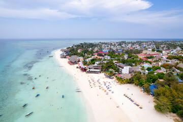 Aerial view of the fishing boats on tropical sea coast with sandy beach at sunset. Summer holiday on Indian Ocean, Zanzibar, Africa. Landscape with boat, buildings, transparent blue water. Top view