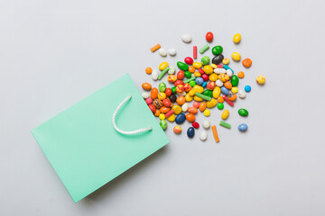 shopping paper gift bag in corner full of assorted traditional candies falling out on colored background with copy space. Happy Holidays sale concept