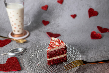 red velvet cake with red hearts and glass of milk on stone gray background with gold cutlery
