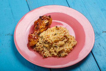 Couscous in sauce and spices with grilled chicken drumstick on a plate on a blue table.