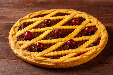 Cherry shortcrust pastry pie decorated with cherries on a wooden table.