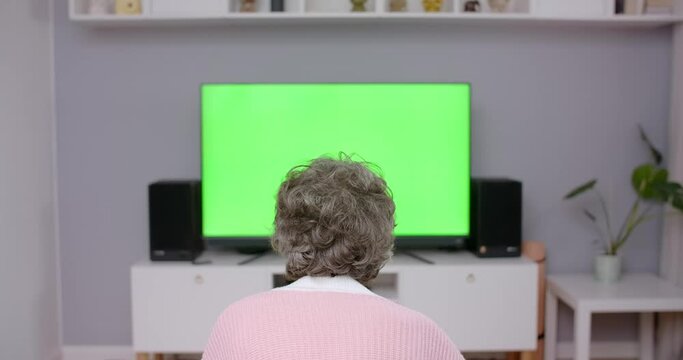 Old lady sits on a couch and turns on TV with greenscreen, chroma key4k