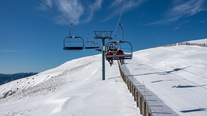Fototapeta na wymiar Lift with chair in a ski resort full of snow on sunny day and blue sky, Andorra, Pyrenees.