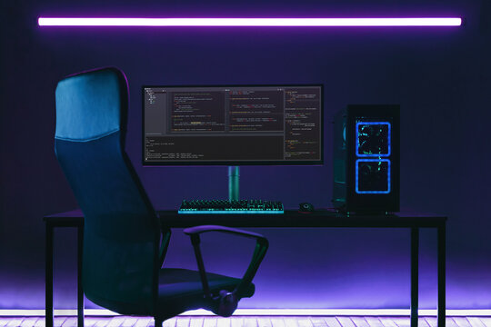 Home office programmer workplace with professional coding setup on desktop. Modern powerful PC and display with programming code in coder studio in neon lights.
