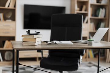 Shot of modern workplace, office with laptop, books, papers, eyeglasses, headset on wood table with large tv on white wall background.