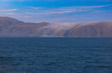 Lake Sevan with mountains in the background partially covered by descending clouds