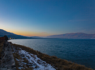 Coastline curve of the lake Sevan at sunset, with mountains in the background