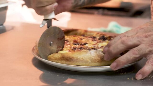 Pizzero con rodillo cortando la pizza reci&eacute;n preparada, mostrando sus manos mientras sujeta la pizza
