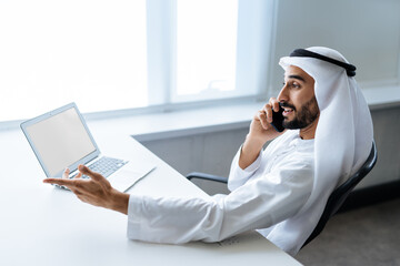 handsome man with dish dasha working in his business office of Dubai. Portraits of a successful businessman in traditional emirates white dress. 