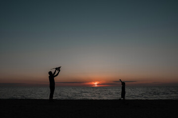 happy family father and child daughter run with kite in the meadow. silhouettes on the background of the sea sunset. High quality photo.