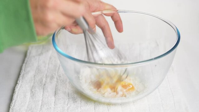 A man beats eggs with a hand whisk in a transparent bowl on the kitchen table. High quality 4k footage