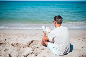 Young man sitting on the beach reading book