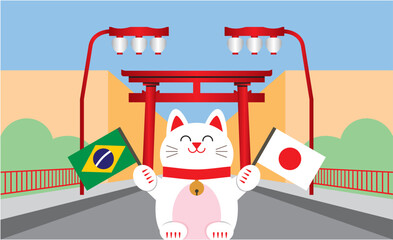 Gato da sorte japonês (maneki neko) segurando bandeiras do Brasil e Japão, simbolizando a amizade entre estes dois países. Ao fundo, portal e lanternas localizados no bairro da Liberdade, em São Paulo
