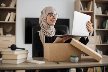 Muslim woman doing live stream while unpacking box with new laptop. Female blogger sharing her feedback about modern gadget with her subscribers.