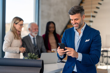 Handsome businessman member of diverse business team holding smartphone using mobile technology checking corporate apps, smiling, looking satisfied.