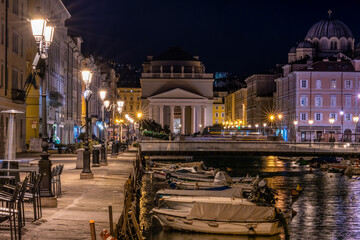 Obraz premium Piazza Sant'Antonio Nuovo in Trieste, Italy. Perspective along the canal with boats at night on the pier
