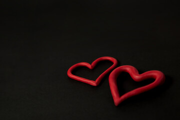 Manos formando corazón el fondo negro y corazones hechos en plastilina, concepto del día del amor...