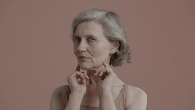 Portrait Of Beautiful 60s Grey-haired Mature Senior Adult Female Posing Without Makeup Against Light Brown Background. Studio Shot, Soft Lighting. No Make Up, Clean Skin. Shot With ARRI Alexa Mini LF