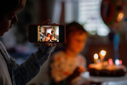 Two beautiful kids, little preschool boys celebrating birthday and blowing candles on homemade baked cake, indoor. Brother making picture with mobile phone.