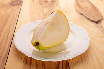 One piece of ripe pear on a white ceramic saucer, close-up, on a wooden table.