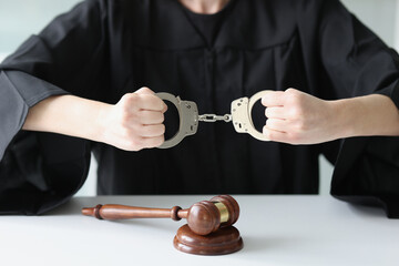 Judge sitting at table with wooden judge gavel and holding handcuffs.