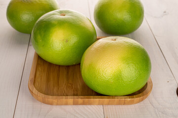 Several organic juicy Citrus Sweetie on a bamboo tray, close-up, on a white wooden table.
