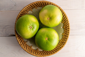 Three juicy organic Citrus Sweetie on a ceramic plate, close-up, on a white wooden table, top view.