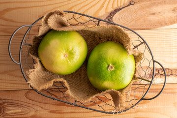 Two juicy organic Citrus Sweetie in a wire basket, close-up, on a wooden table, top view.