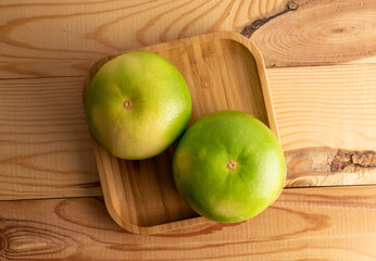 Two juicy organic Citrus Sweetie in a bamboo dish, close-up, on a wooden table, top view.