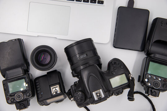 top view of work space photographer with digital camera, flash, cleaning kit, memory card, external hard disk, USB card reader, laptop and camera accessory on white table background
