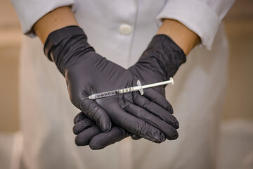 Sao Paulo, SP, Brazil - January 22 2023: Person in white coat and black gloves holding syringe with needle details.
