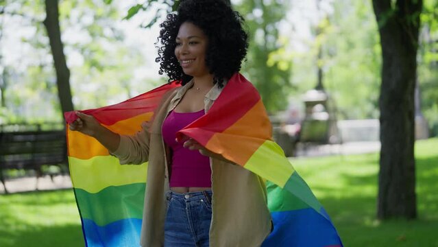 Cheerful African American woman holding rainbow flag in park, lgbt movement