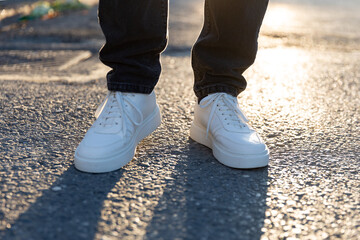 Man in white sneakers shoes on asphalt at sunset. Men's shoes