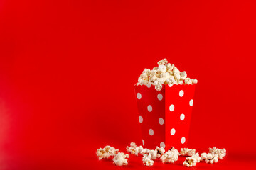 Popcorn in a red bag with white polka dots on a red background. Front view, copy space.