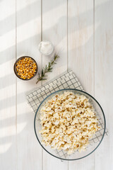 bowl with popcorn, popcorn kernels and salt on a checkered napkin , on a white wooden table, top view