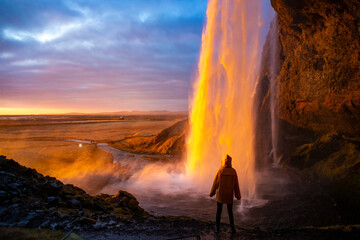 Girl in yellow raincoat admires the stunning colorful sunset spectacle from behind the impressive...