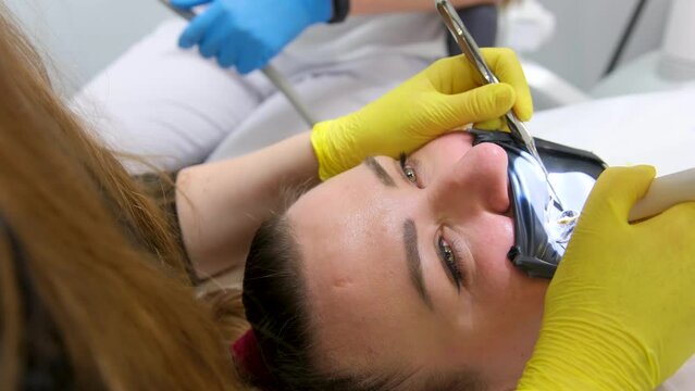 cofferdam clamp for cofferdam The process of dental prosthetics using microscope, female doctor in yellow gloves, patient dentist with patient, using dental curing light