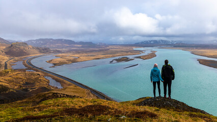 romantic photo of a pair of hikers admiring Iceland's rugged landscape from the top of a mountain; a panorama of glacial lakes and mountains