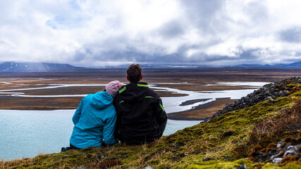 Naklejka na ściany i meble romantic photo of a pair of hikers admiring Iceland's rugged landscape from the top of a mountain; a panorama of glacial lakes and mountains