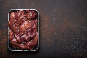 Raw chicken liver in black supermarket tray top view on dark rustic concrete background kitchen table. Healthy food ingredient, source of iron, folate, vitamins and minerals. Space for text